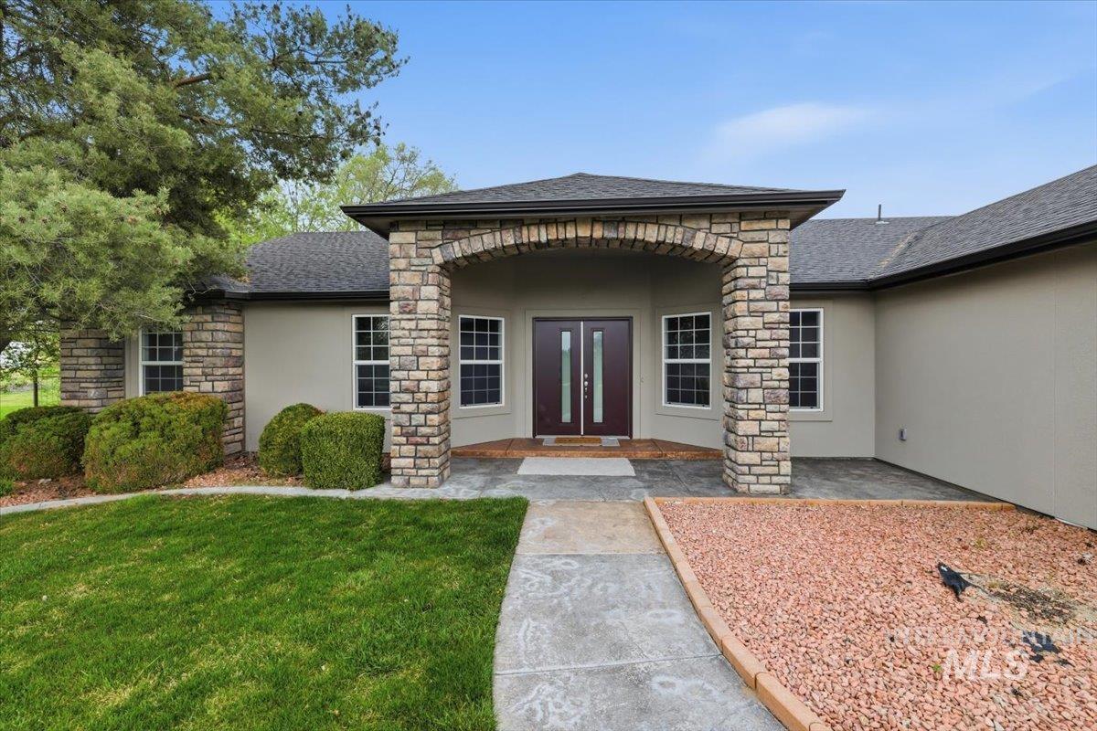 25022 Tumbleweed Road Middleton, ID 83644 - Photo 1 of 41 Doorway to property featuring stucco siding, stone siding, a lawn, and a shingled roof