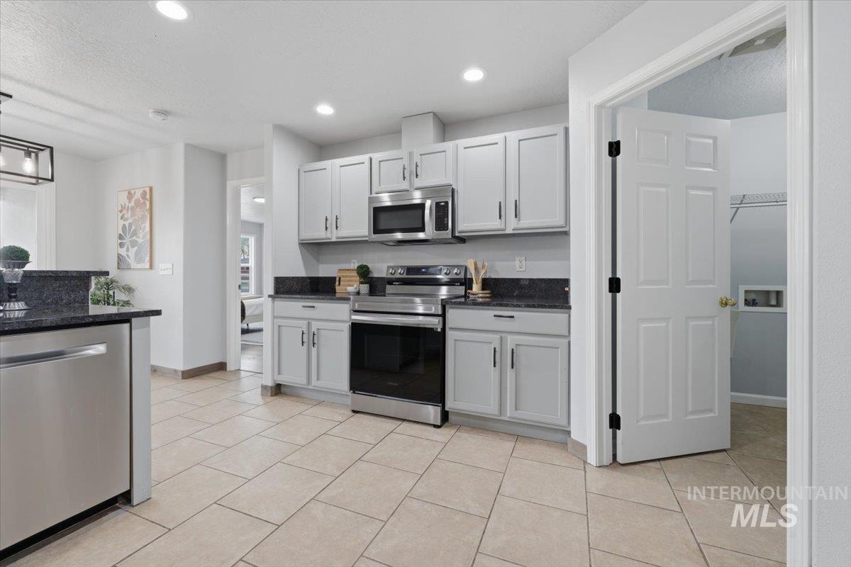 25022 Tumbleweed Road Middleton, ID 83644 - Photo 13 of 41 Kitchen with stainless steel appliances, dark stone counters, light tile patterned flooring, pendant lighting, and a textured ceiling