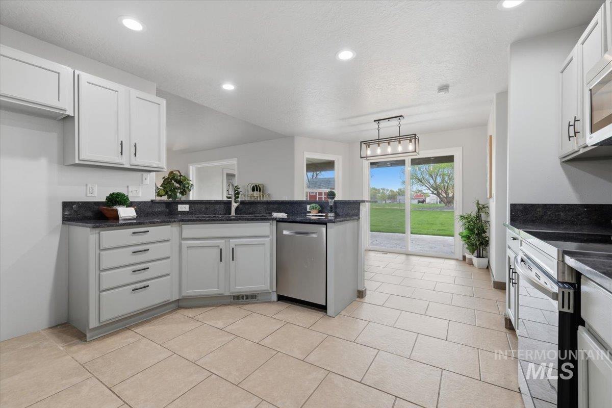 25022 Tumbleweed Road Middleton, ID 83644 - Photo 14 of 41 Kitchen with a peninsula, stainless steel appliances, pendant lighting, dark stone counters, and white cabinetry