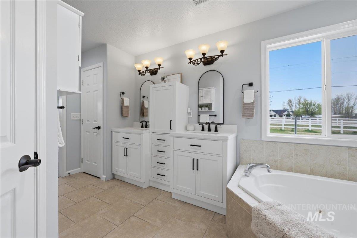 25022 Tumbleweed Road Middleton, ID 83644 - Photo 18 of 41 Full bathroom with two vanities, a jetted tub, a textured ceiling, and light tile patterned floors