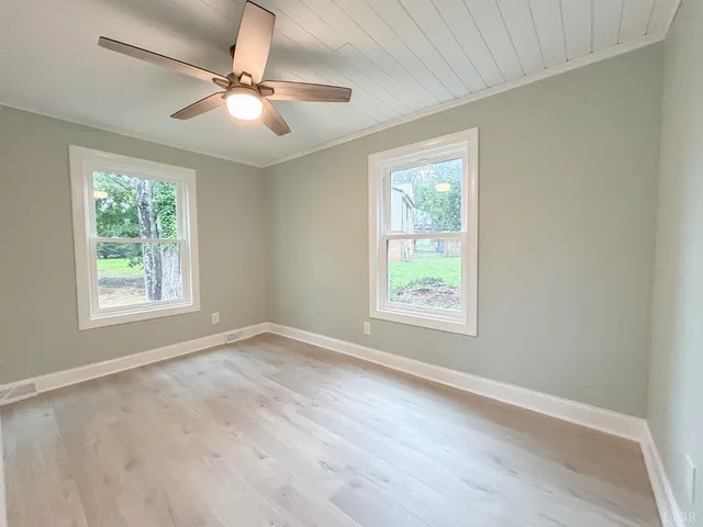 an empty room with wooden floor fan and windows