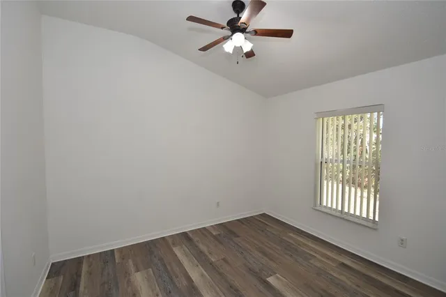 an empty room with wooden floor chandelier fan and windows