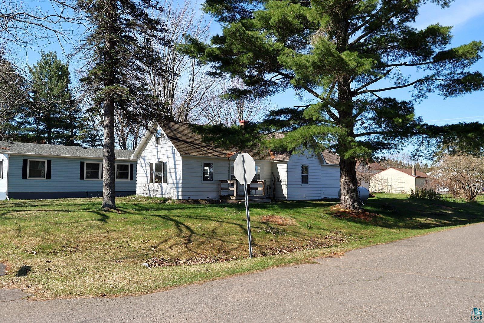 83185 Washington Avenue Port Wing, WI 54865 - Photo 23 of 26 White siding exterior with a pitched roofline, surrounded by mature trees and a green lawn