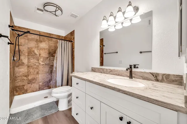 a bathroom with a granite countertop sink a toilet a mirror a bathtub and shower