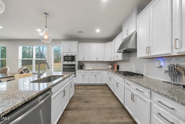 a kitchen with stainless steel appliances granite countertop a dining table chairs sink and cabinets