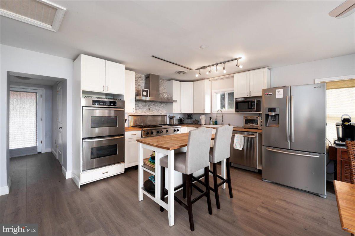 1312 Tuggies Road Pasadena, MD 21122 - Photo 10 of 75 a kitchen with stainless steel appliances a refrigerator a stove a sink and white cabinets with wooden floor
