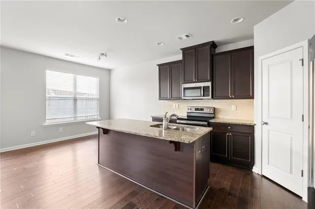 a kitchen with stainless steel appliances granite countertop a stove a sink dishwasher a refrigerator and a microwave oven with wooden floor