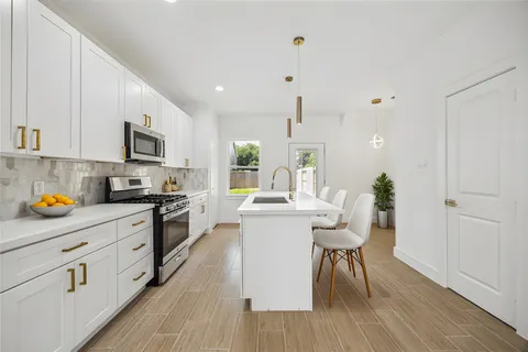 a kitchen with stainless steel appliances kitchen island granite countertop a stove a sink a refrigerator and white cabinets with wooden floor