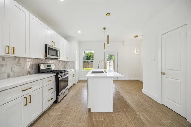 a large kitchen with stainless steel appliances granite countertop a stove top oven a sink dishwasher and a refrigerator with wooden floor