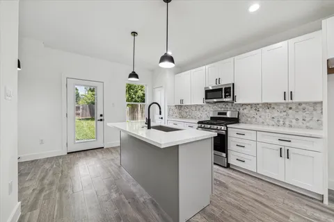a kitchen with stainless steel appliances white cabinets a sink a stove a microwave and wooden floors