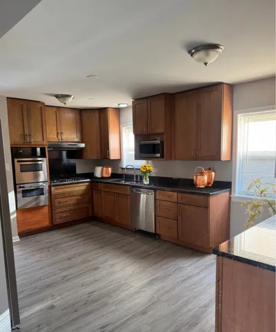 a kitchen with granite countertop wooden floors stainless steel appliances and window
