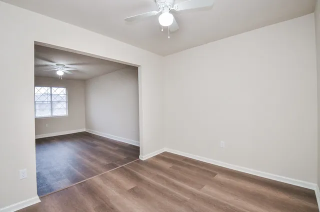 an empty room with wooden floor chandelier fan and windows