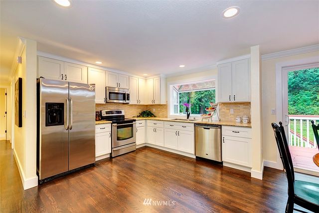 a kitchen with a refrigerator a stove top oven a sink dishwasher a dining table and chairs with wooden floor