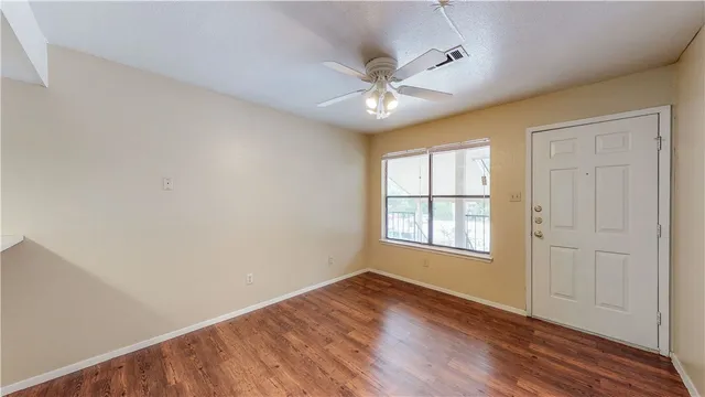 an empty room with wooden floor fan and windows