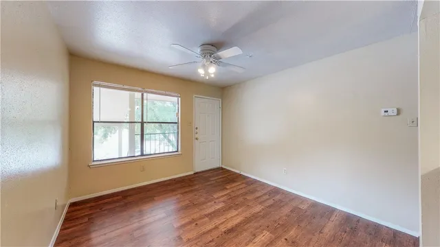 an empty room with wooden floor ceiling fan and windows