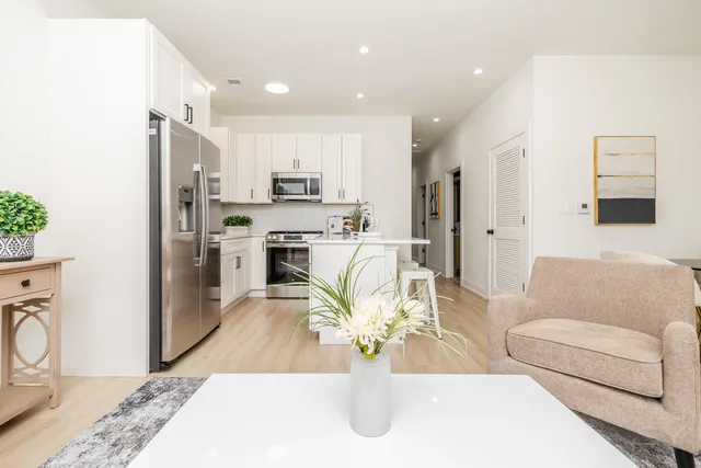 a living room with stainless steel appliances furniture a rug and a kitchen view