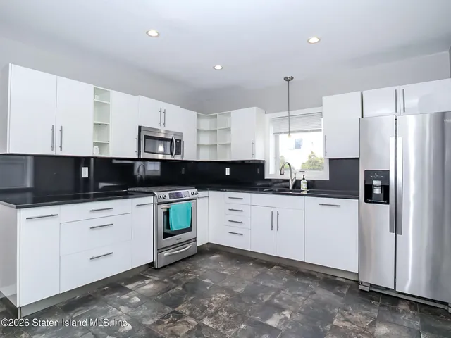 a kitchen with stainless steel appliances white cabinets a sink a stove a refrigerator and white cabinets