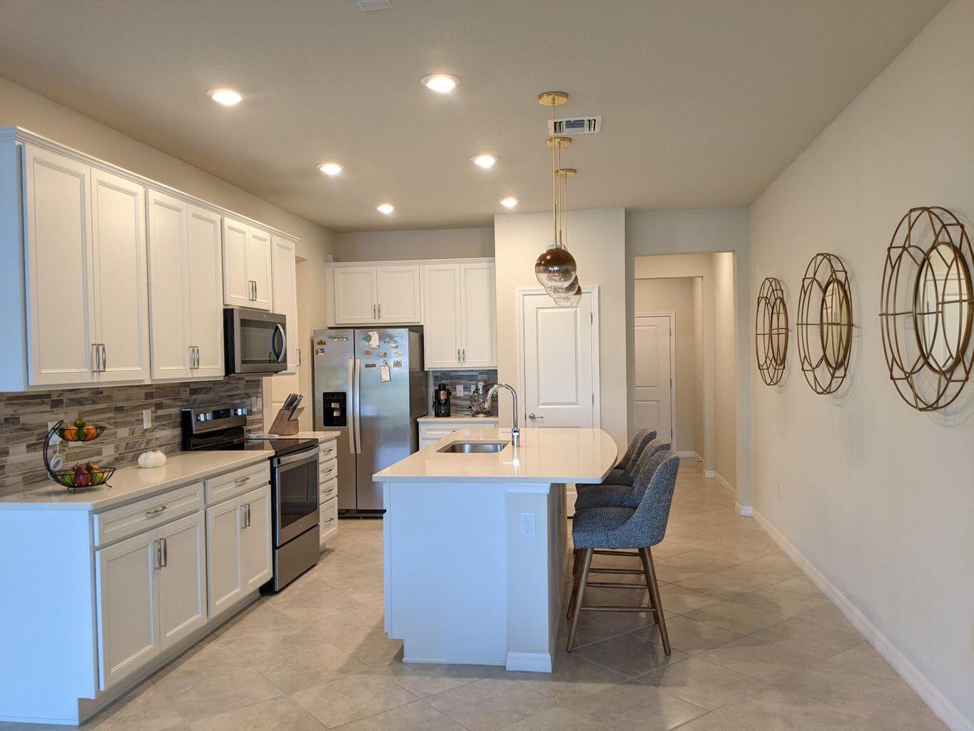 a open kitchen with stainless steel appliances granite countertop a stove top oven a sink dishwasher a refrigerator and white cabinets with wooden floor