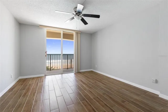 a view of an empty room with wooden floor and a ceiling fan