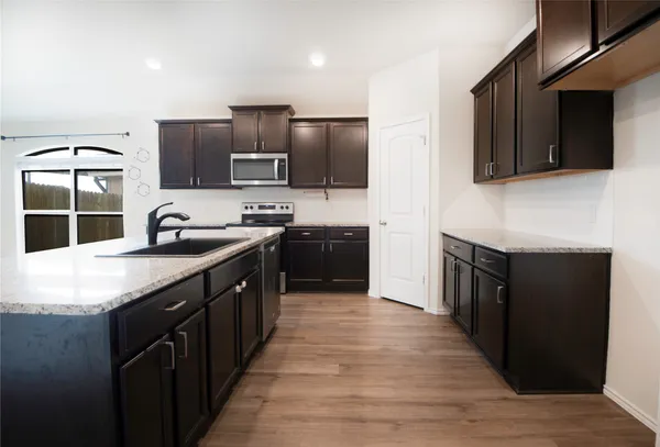 a kitchen with stainless steel appliances a sink dishwasher a stove top oven a refrigerator with wooden cabinets and floor