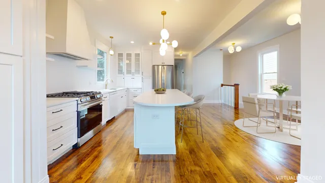 a kitchen with stainless steel appliances kitchen island granite countertop a stove a sink dishwasher a dining table and chairs with wooden floor