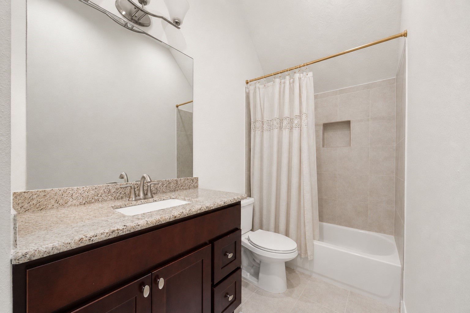 1904 Boulder Ridge Drive Conroe, TX 77304 - Photo 30 of 37 This pristine secondary bathroom offers a functional layout featuring a rich dark wood vanity with a premium granite countertop and an undermount sink. The space is complete with a clean tub-and-shower combination accented by a neutral tile surround and a convenient built-in shampoo niche.