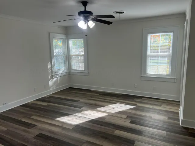 an empty room with wooden floor chandelier fan and windows
