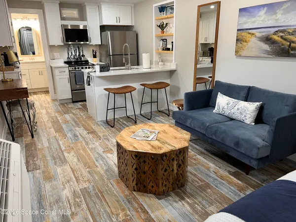 a living room with stainless steel appliances furniture a rug and a kitchen view