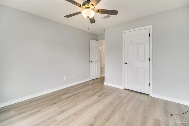 an empty room with wooden floor fan and windows