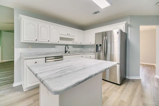 a kitchen with stainless steel appliances granite countertop a refrigerator a sink a stove and white cabinets with wooden floor