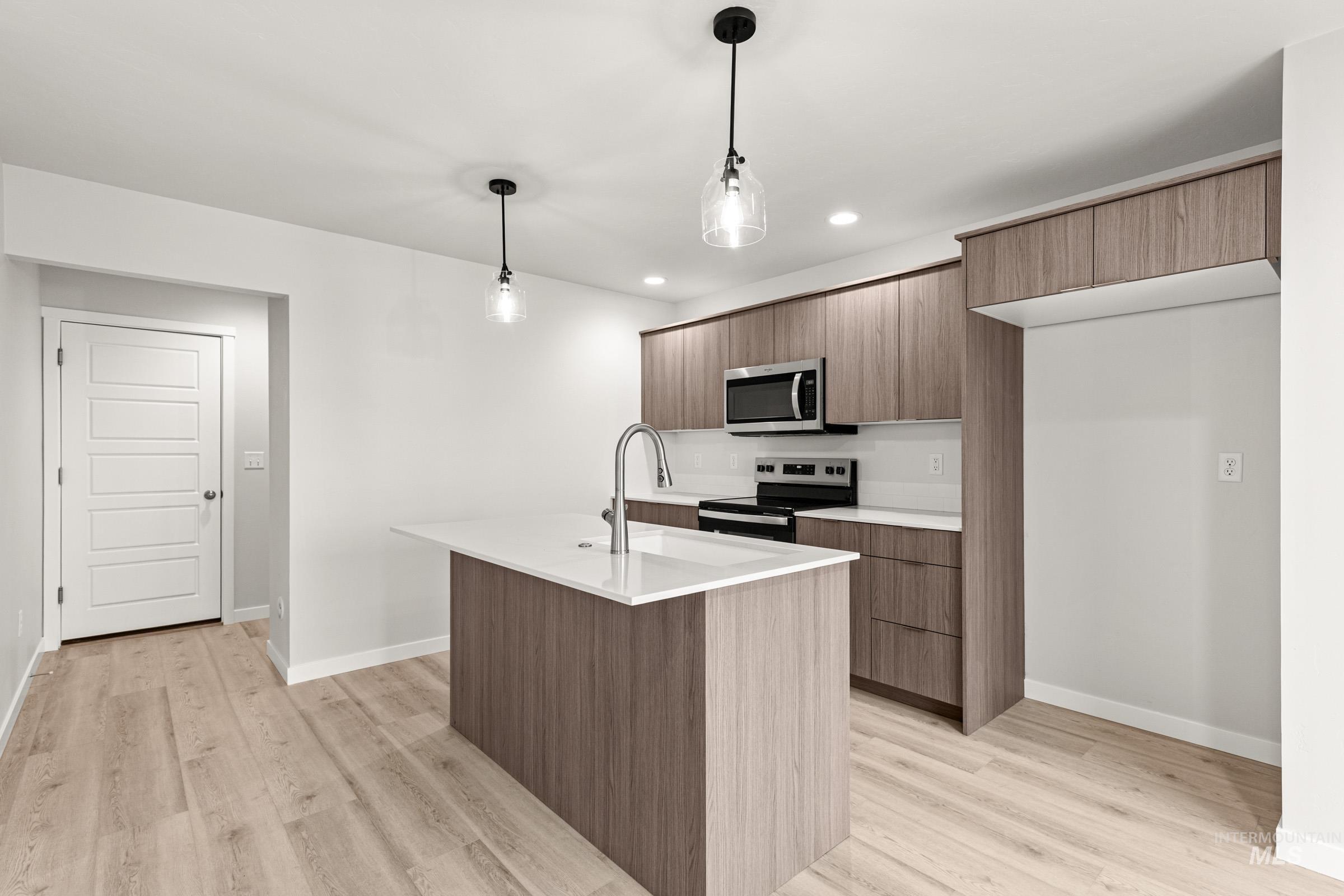 10818 Rutland Street Caldwell, ID 83605 - Photo 5 of 22 Kitchen featuring stainless steel appliances, hanging light fixtures, an island with sink, light wood finished floors, and modern cabinets