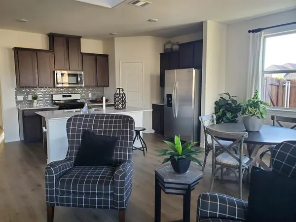 a kitchen with stainless steel appliances granite countertop a refrigerator a stove a sink dishwasher a dining table and chairs with wooden floor