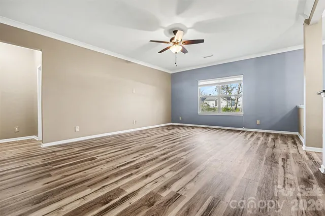 an empty room with wooden floor chandelier fan and windows