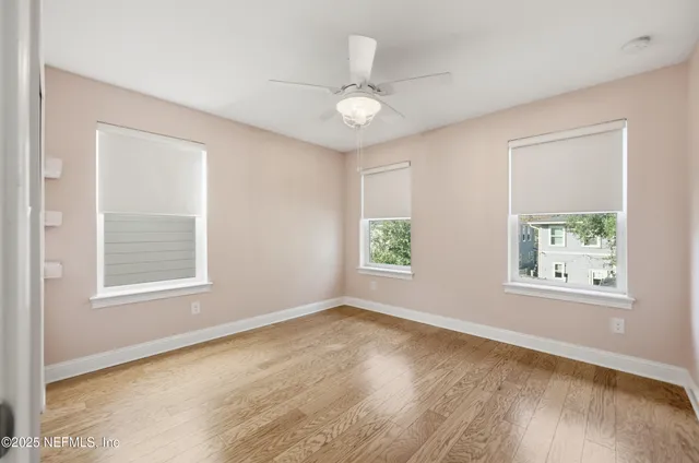 an empty room with wooden floor chandelier fan and windows