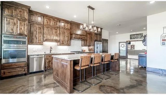 a kitchen with stainless steel appliances kitchen island granite countertop a table chairs sink and cabinets