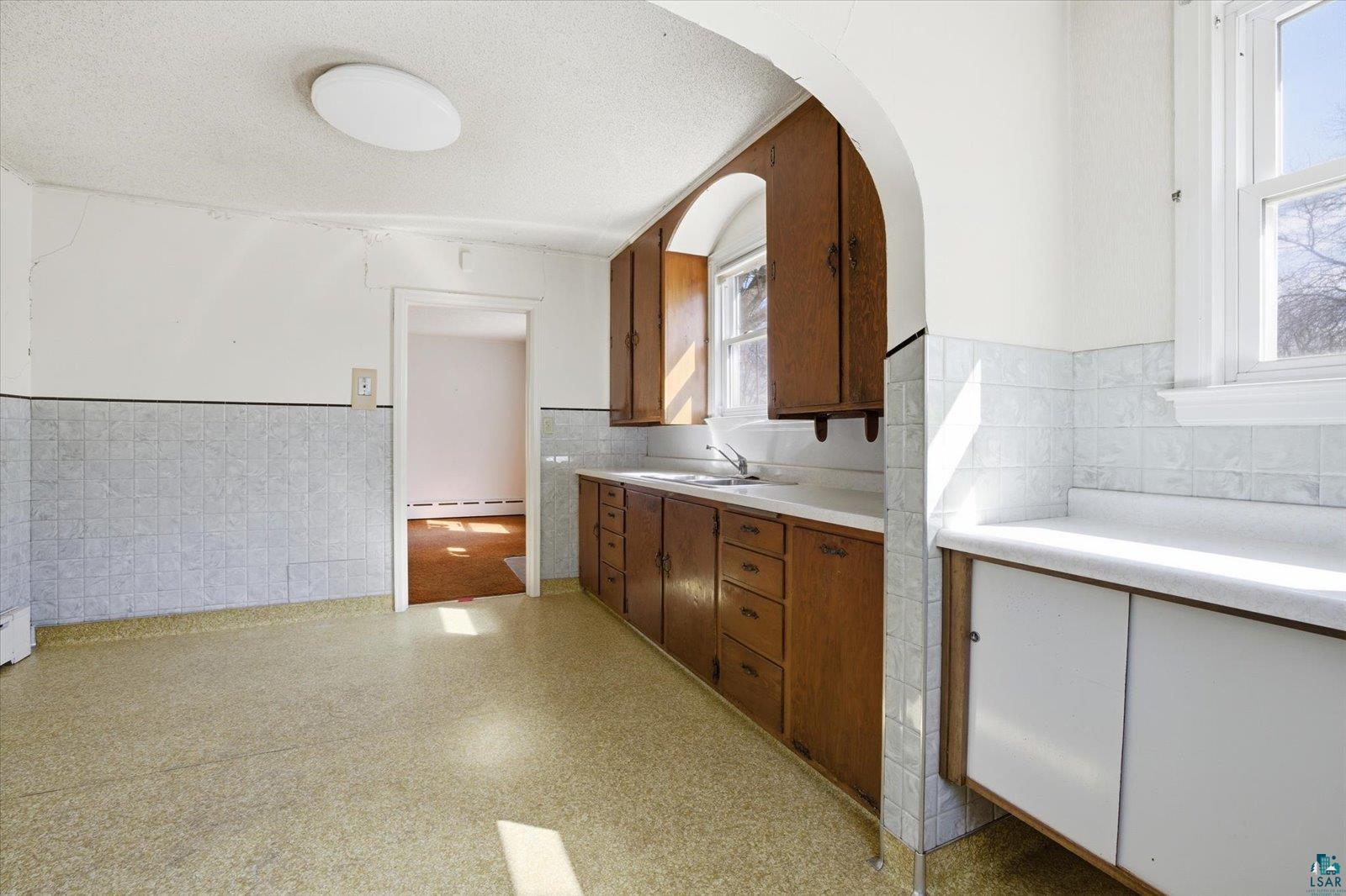 709 Michigan Street Hibbing, MN 55746 - Photo 34 of 47 Kitchen with a wainscoted wall, light countertops, wood finish cabinets, tile walls, and a baseboard heating unit