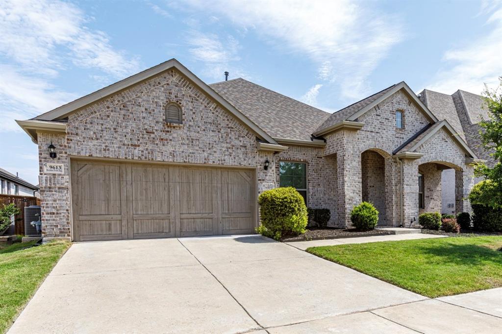 9613 Boulder Pt Road Oak Point, TX 75068 - Photo 2 of 28 Brick exterior featuring a two-car garage with wood-paneled doors, arched entryways, and a concrete driveway