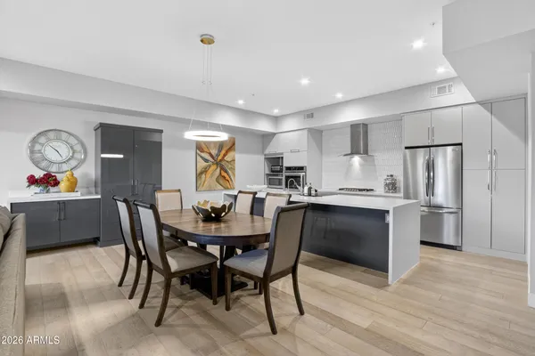 a kitchen with stainless steel appliances granite countertop a dining table chairs refrigerator and sink