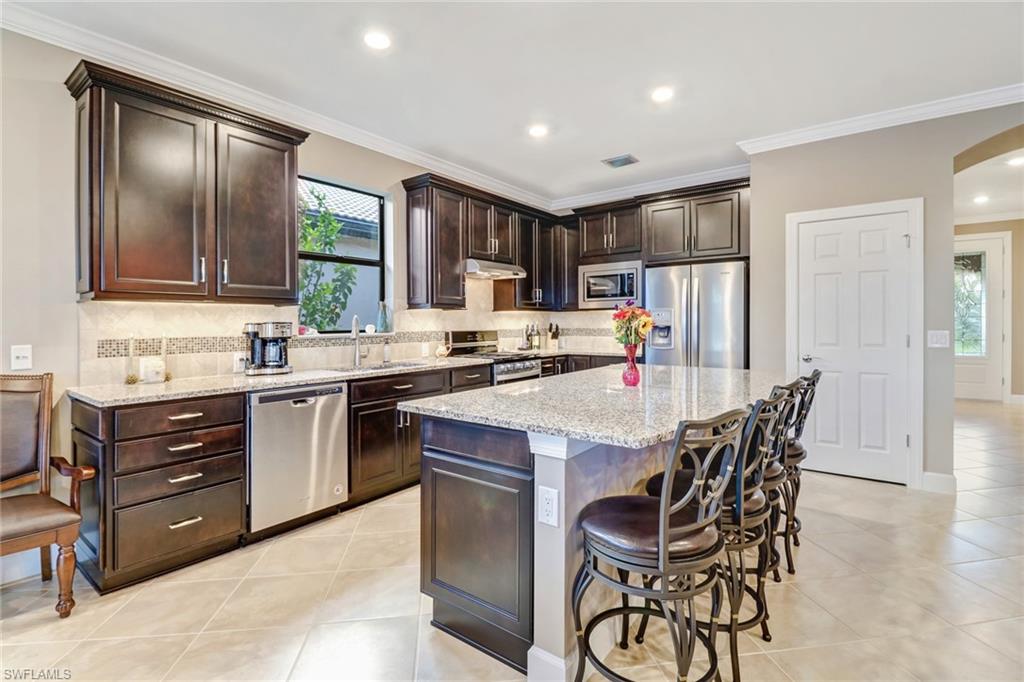 7567 Winding Cypress Drive Naples, FL 34114 - Photo 8 of 24 a kitchen with a stove a sink a refrigerator and chairs