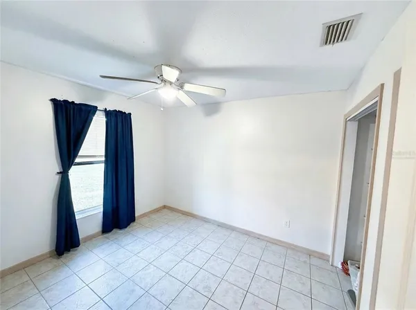 a view of an empty room with window and chandelier fan
