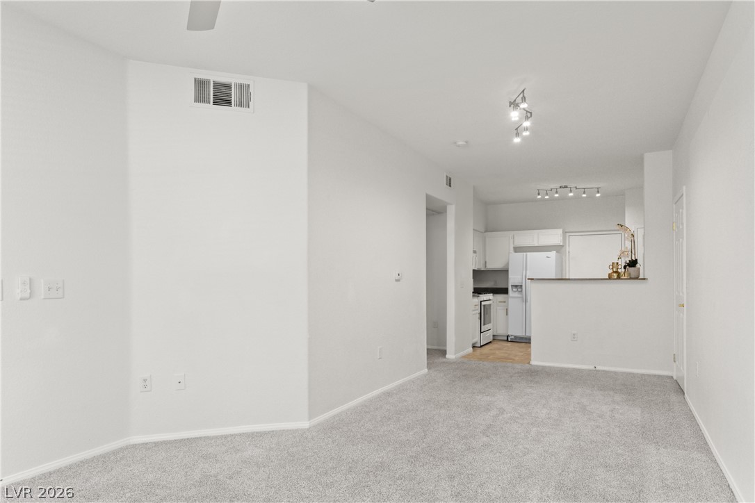 10550 West Alexander Road, Unit 1025 Las Vegas, NV 89129 - Photo 3 of 42 A well-lit living area flows seamlessly into the kitchen, showcasing modern track lighting and neutral carpeting.