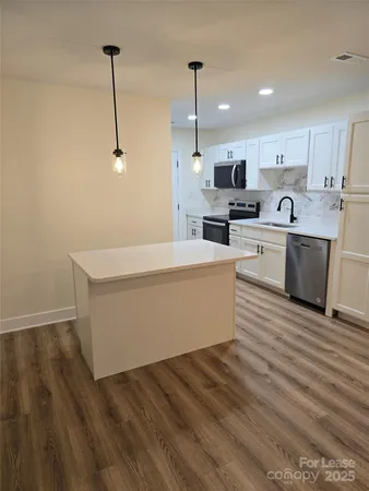 a living room with stainless steel appliances kitchen island granite countertop a sink a stove and white cabinets