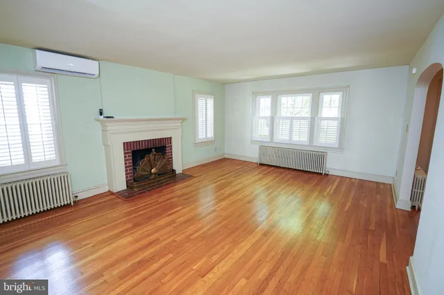 an empty room with wooden floor fireplace and windows