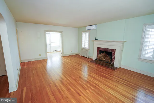an empty room with wooden floor fireplace and windows