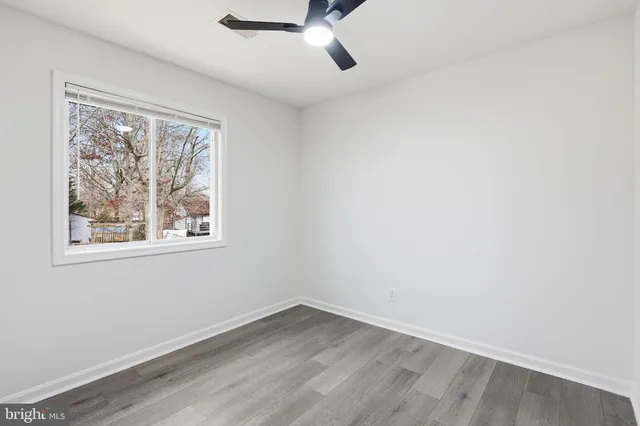 an empty room with wooden floor chandelier fan and windows