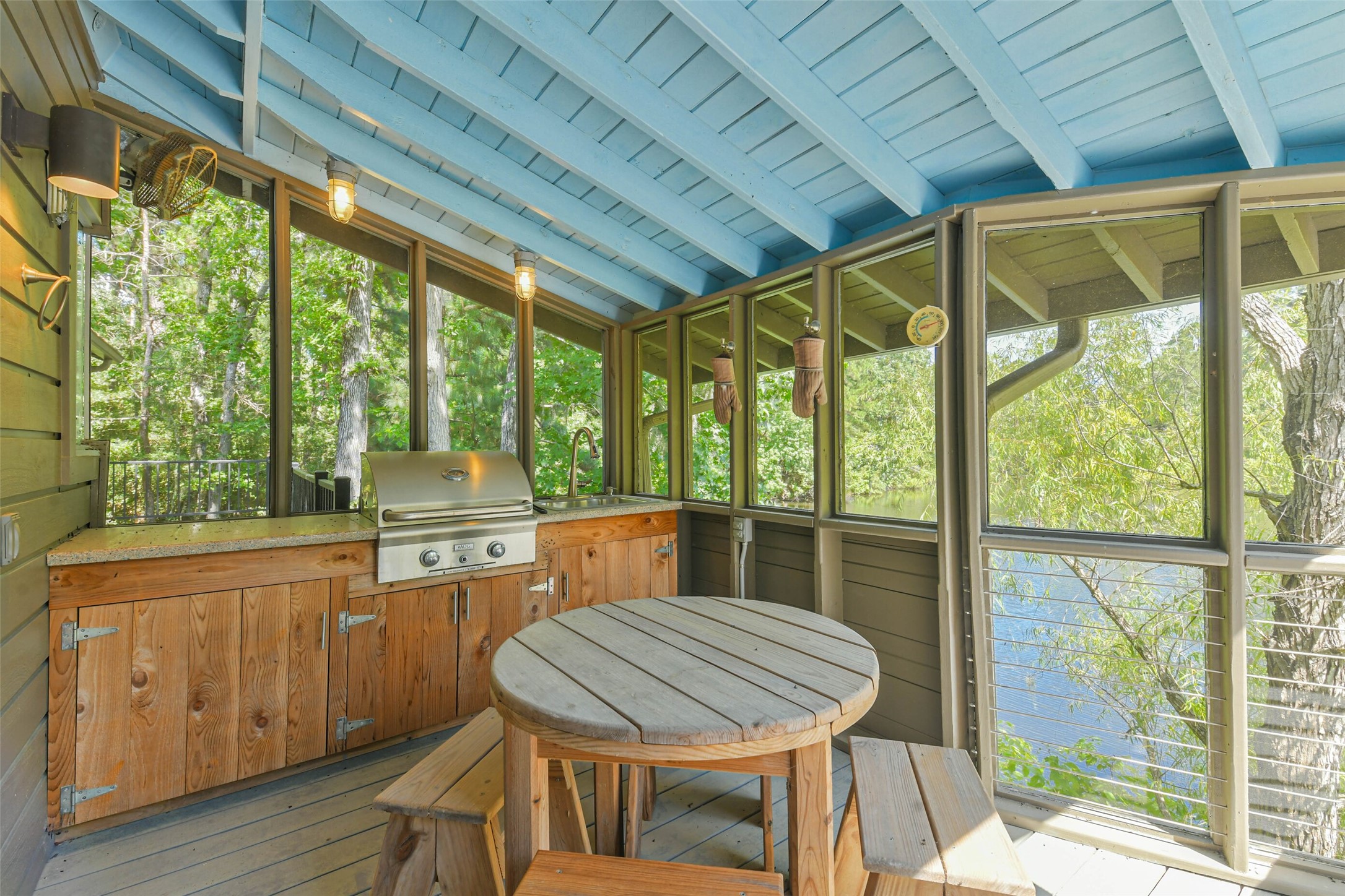 88 Raccoon Ramble Cleveland, TX 77327 - Photo 39 of 43 Charming screened-in porch with a rustic outdoor kitchen and grill, offering serene views of lush greenery and a nearby lake.