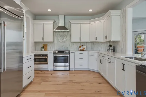 a kitchen with stainless steel appliances granite countertop a sink a stove and white cabinets with wooden floor