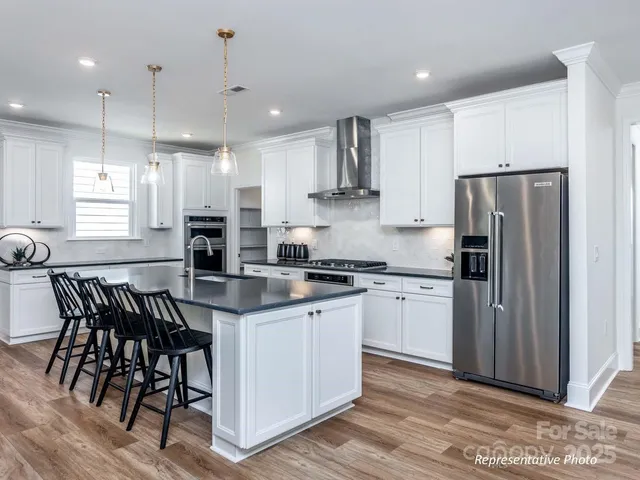 a kitchen with stainless steel appliances granite countertop white cabinets a refrigerator a stove a sink and chairs