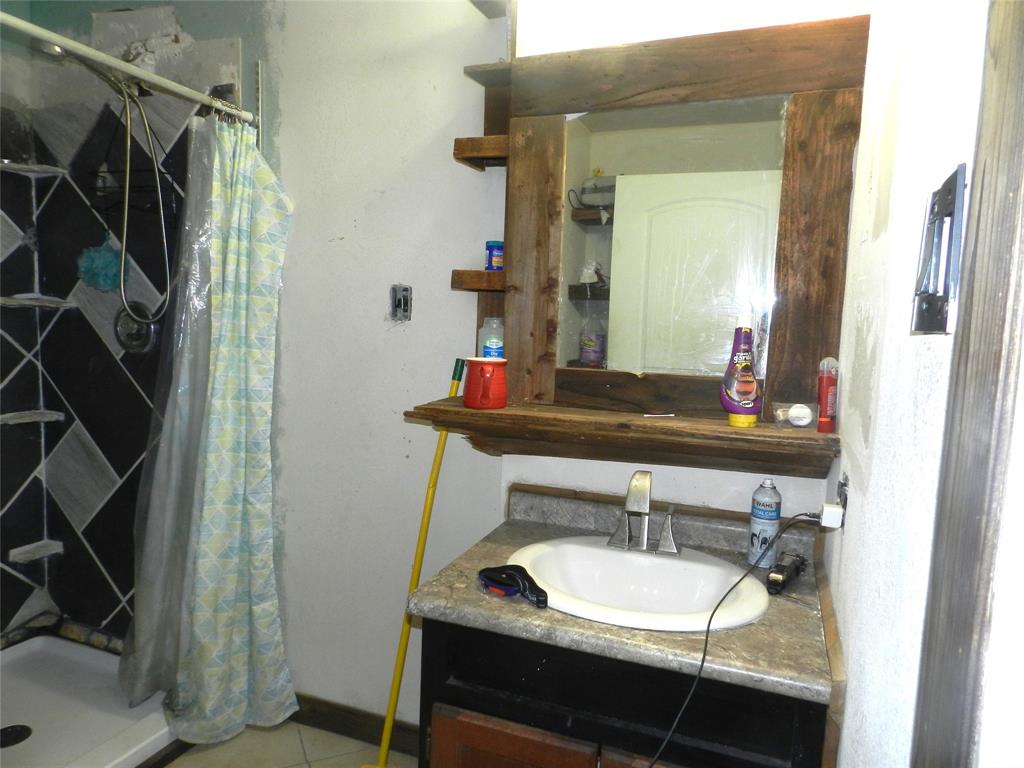 588 Salt Creek Road Springtown, TX 76082 - Photo 17 of 19 Vanity with a white oval sink, chrome faucet, and a wood-framed mirror with integrated shelving