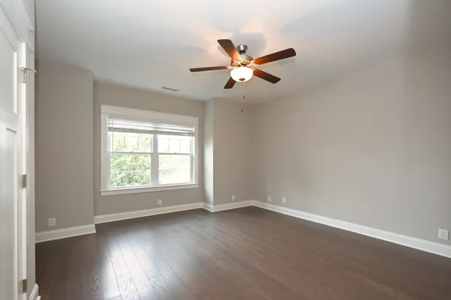 an empty room with wooden floor fan and windows